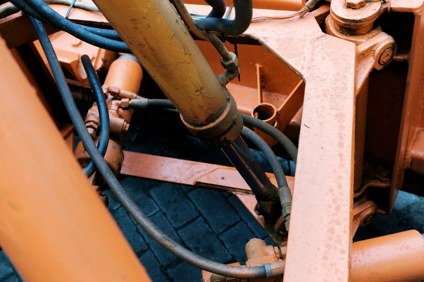 Pomarańczowa maszyna hydrauliczna z centralnym tłokiem i grubymi wężami.